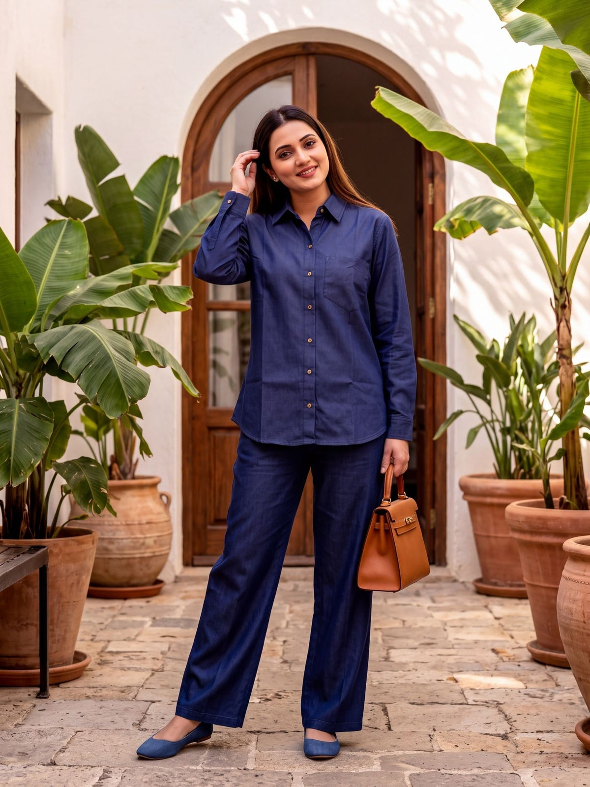 Woman styling the Rivelle Muse deep-indigo denim shirt and palazzo co-ord set in a courtyard